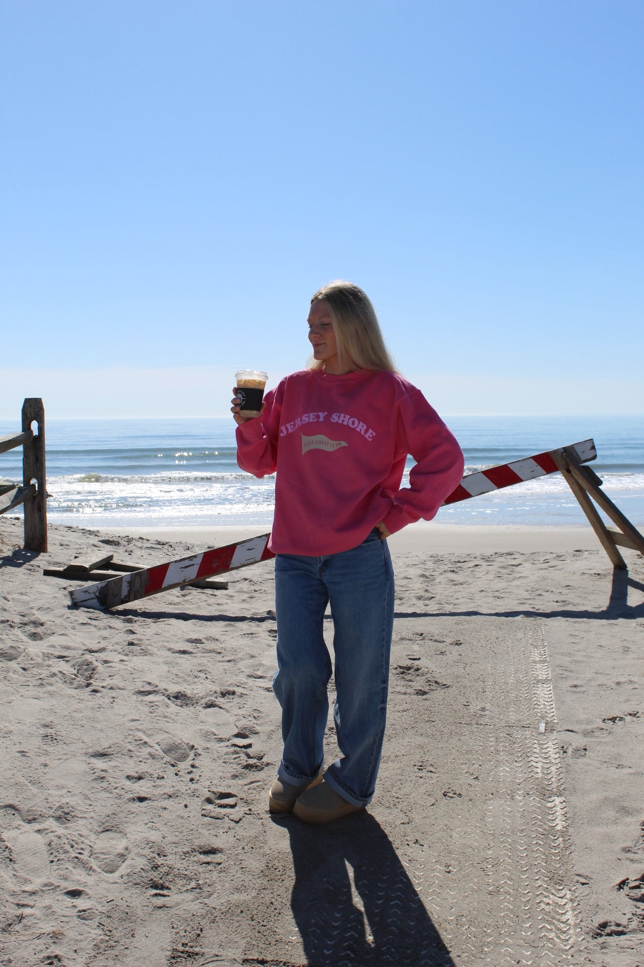 Person wearing a crewneck with "jersey shore" across chest, standing on a sandy beach.