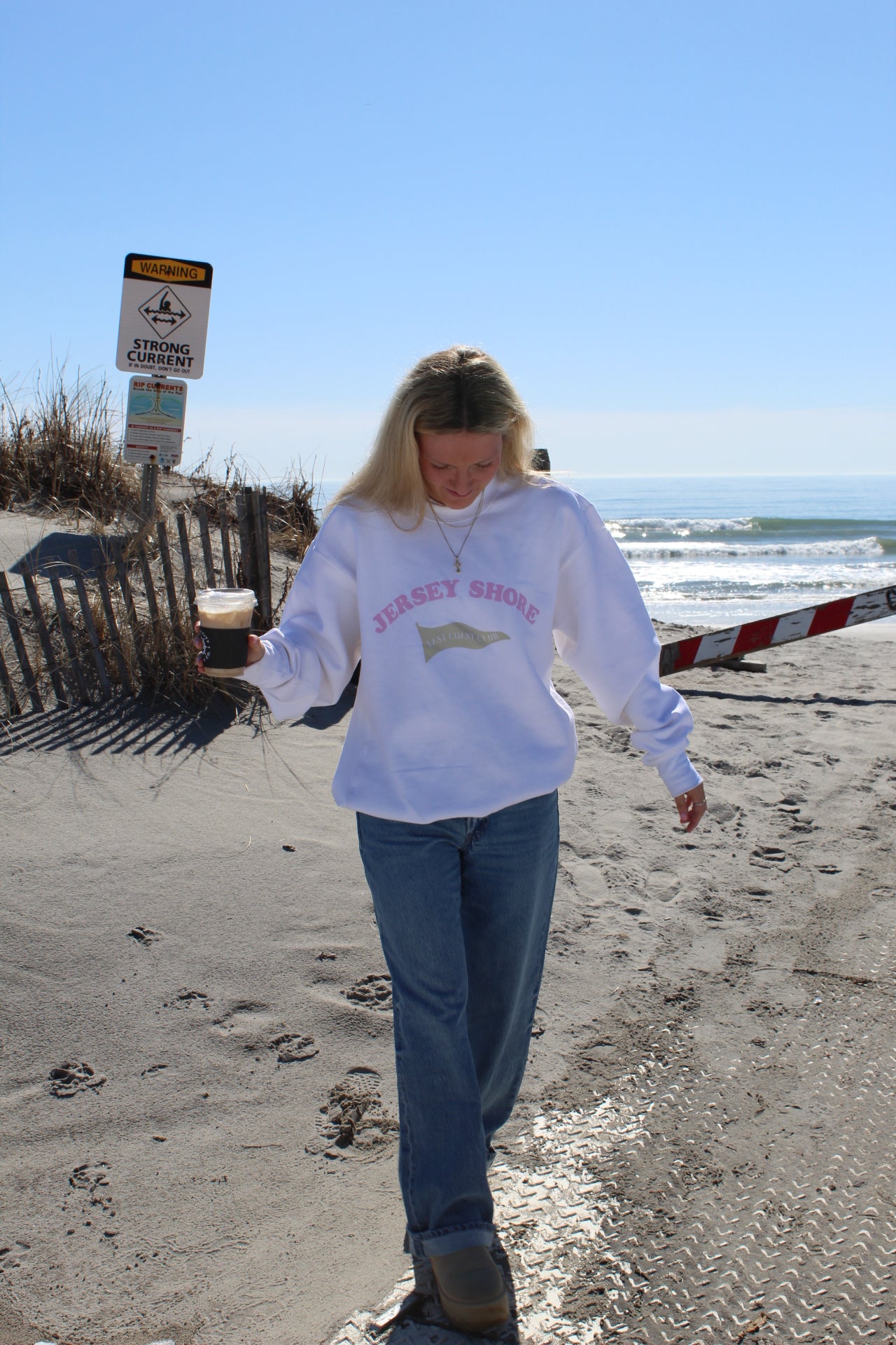 Person wearing a crewneck with "jersey shore" across chest, standing on a sandy beach.