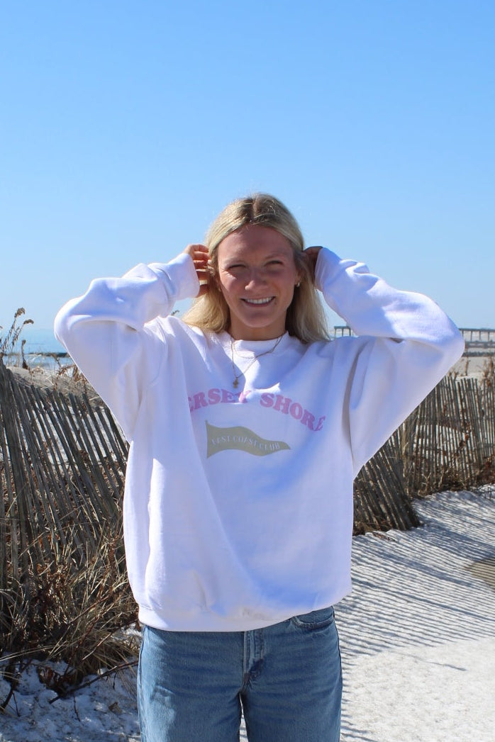 Person wearing a crewneck with "jersey shore" across chest, standing on a sandy beach.