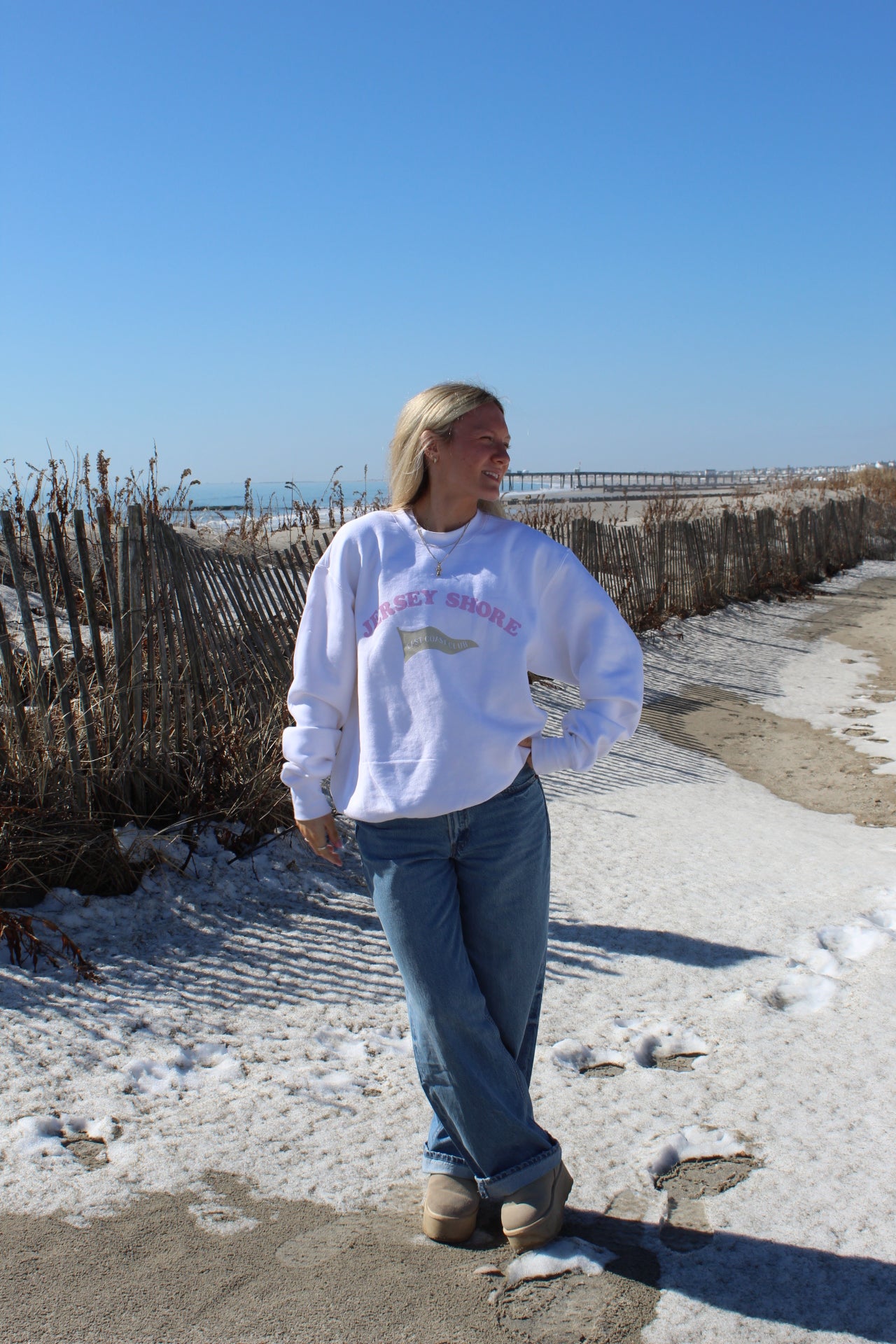 Person wearing a white sweatshirt with a logo on a beach