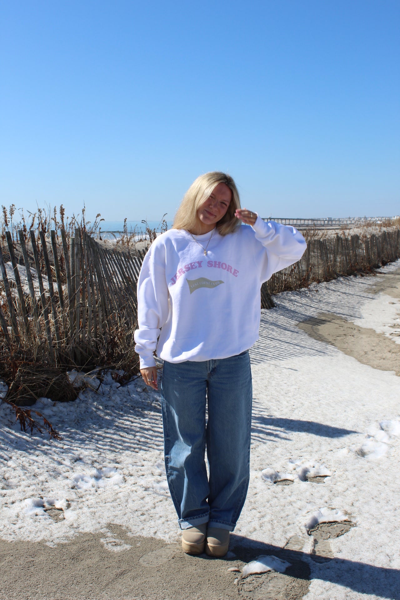 Person wearing a crewneck with "jersey shore" across chest, standing on a sandy beach.